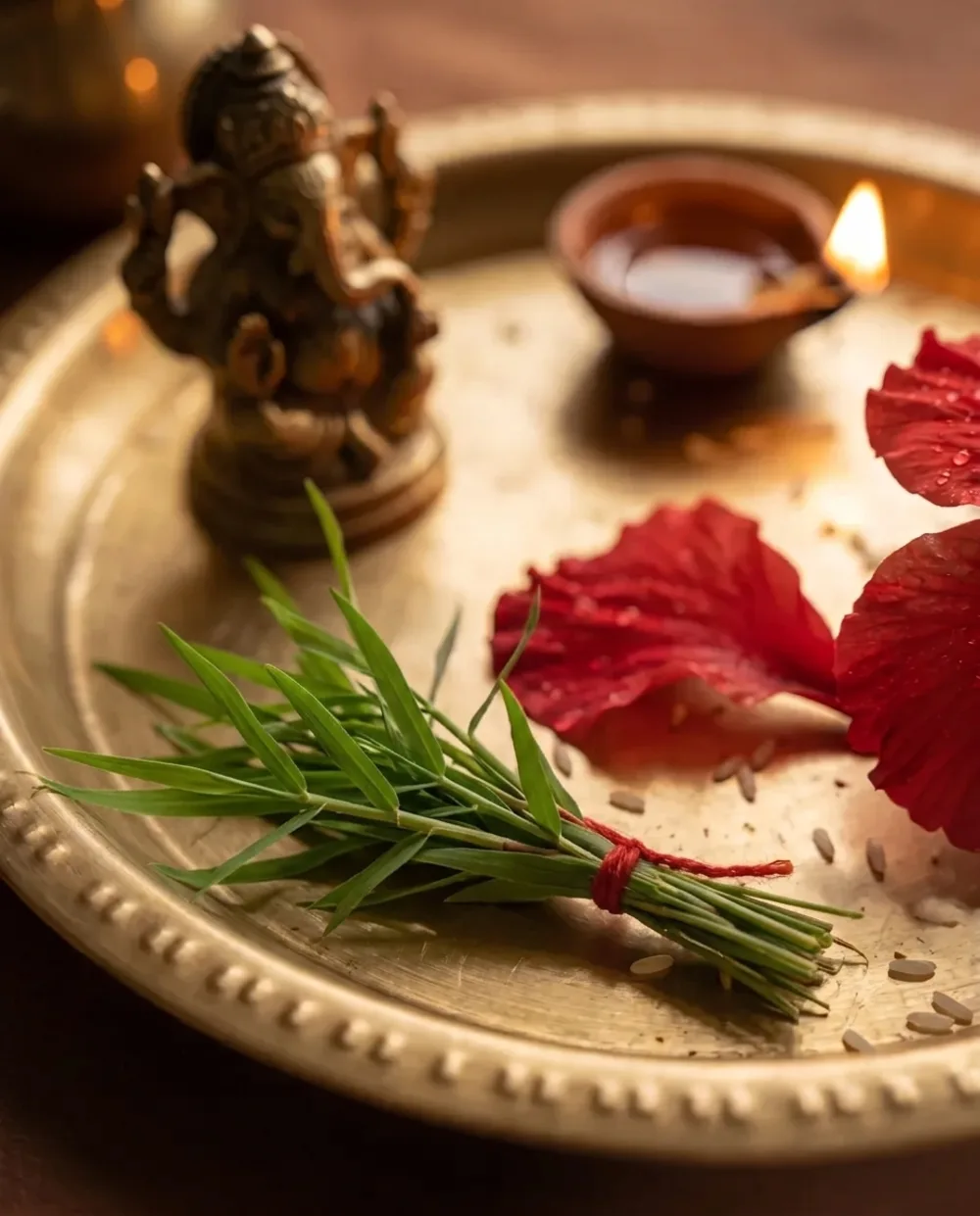 A small bunch of short durva grass sprigs tied with red thread on a brass puja plate, a small brass Ganesha behind